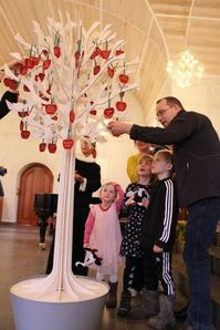 Familie står omkring kirkens dåbstræ og tager deres æble ned.